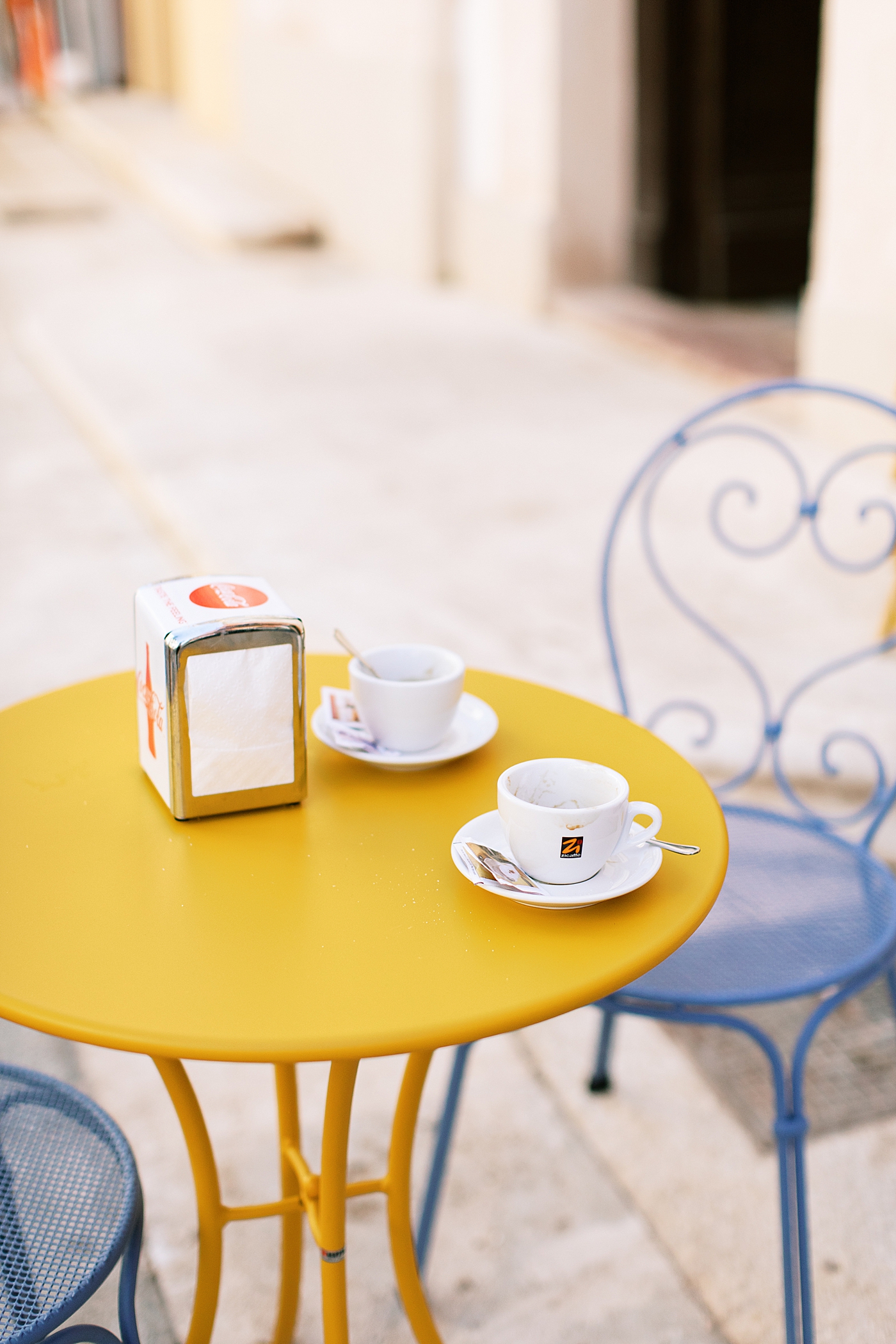 A yellow table with blue chairs and cappuccino mugs | Photo by Josie Derrick 